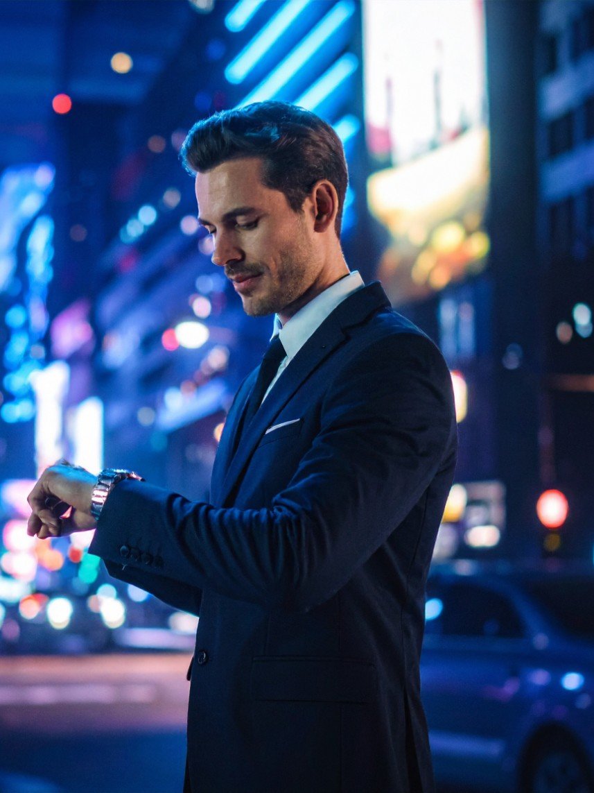 An executive checking his watch on a city street at night